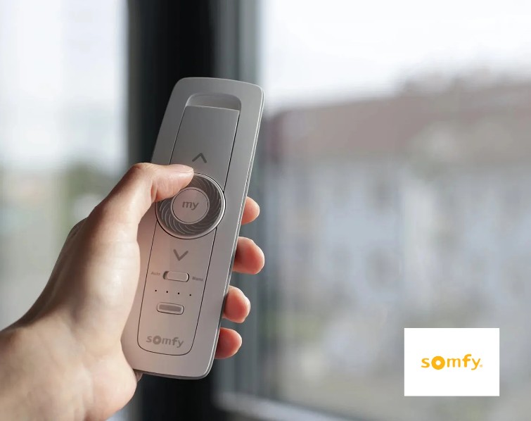Main tenant une télécommande Somfy près d'une fenêtre